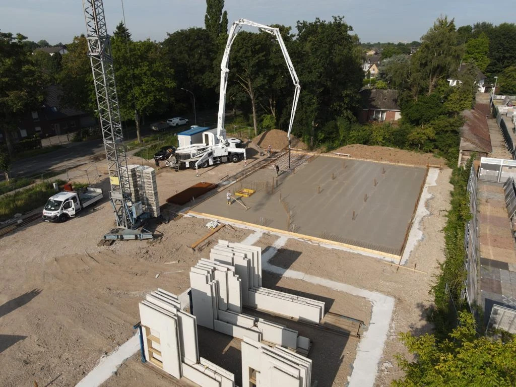 Betonpumpe an einer frisch betonierten Bodenplatte, davor gelagerte Wandelemente